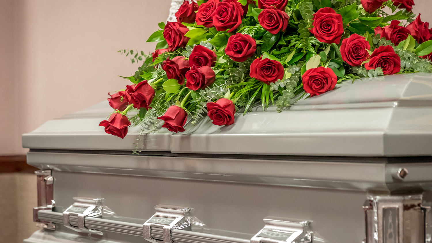 A silver casket with many roses on top.