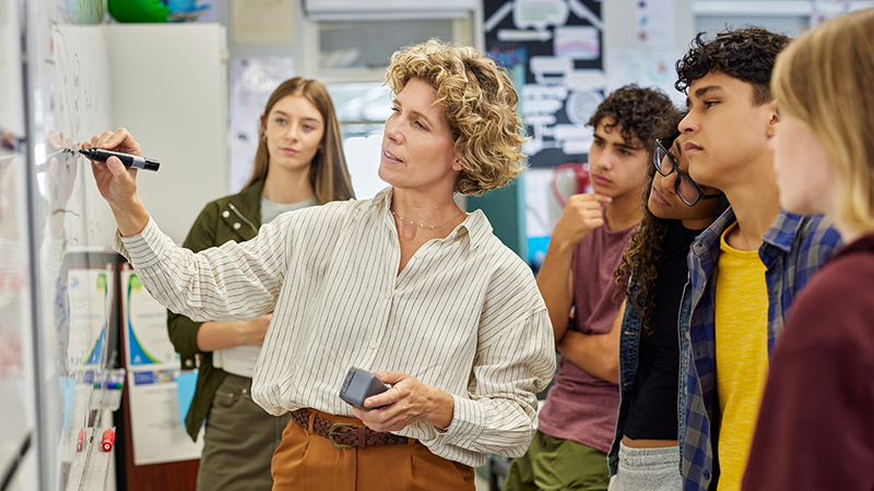 Teacher writes on a white board as students learn